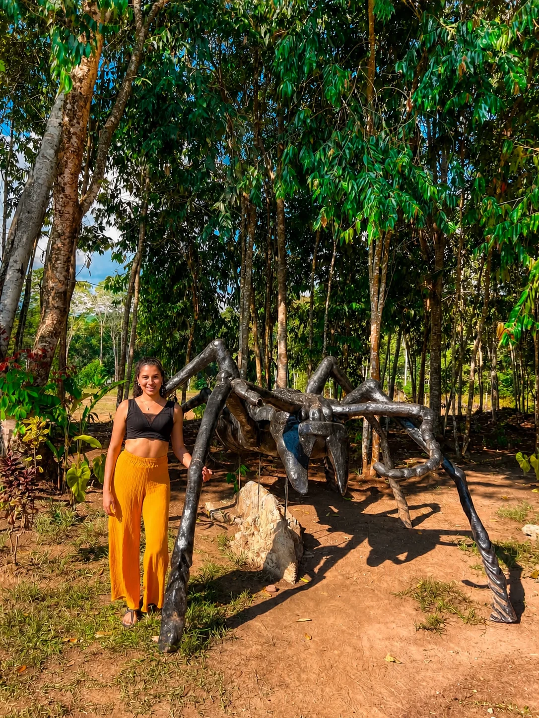 Visitante posando junto a la escultura de una araña gigante entre los árboles