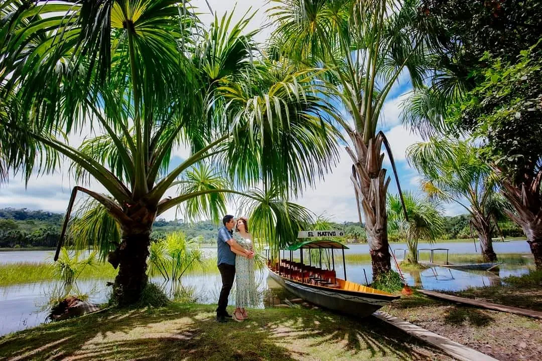 Pareja junto al bote de El Nativo bajo palmeras frente a la laguna
